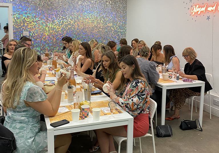 Group pottery painting at long tables with glittery wall in background